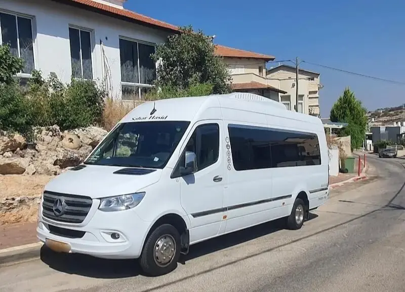 מיניבוס בפריסה ארצית - זווית רחבה של מיניבוס מרצדס לבן חונה בשכונת מגורים באור יום.